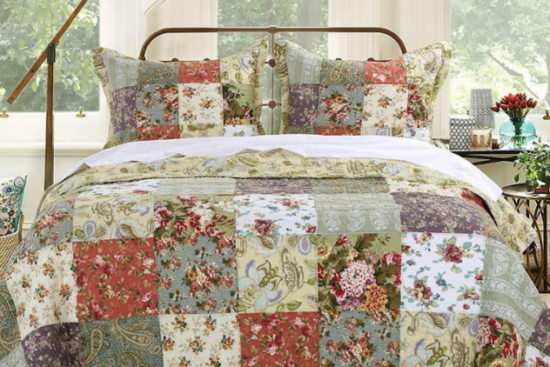 A cozy bedroom with a patchwork quilt featuring floral and paisley patterns in warm tones, set on a vintage-style metal bed frame with natural light streaming in.