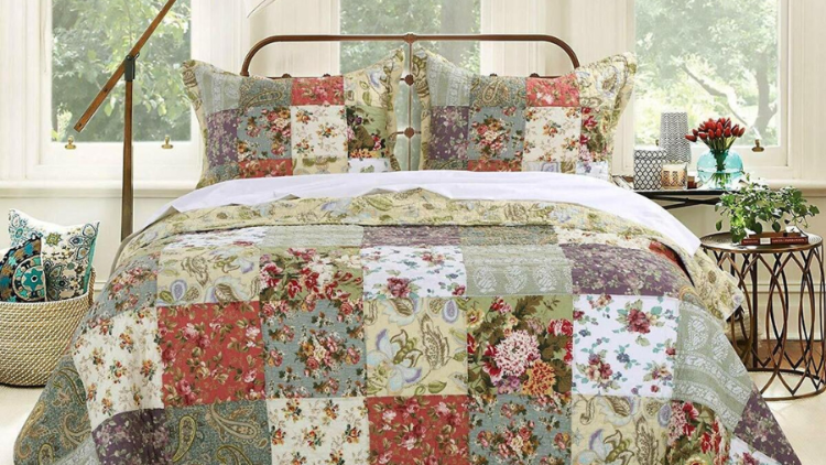 A cozy bedroom with a patchwork quilt featuring floral and paisley patterns in warm tones, set on a vintage-style metal bed frame with natural light streaming in.