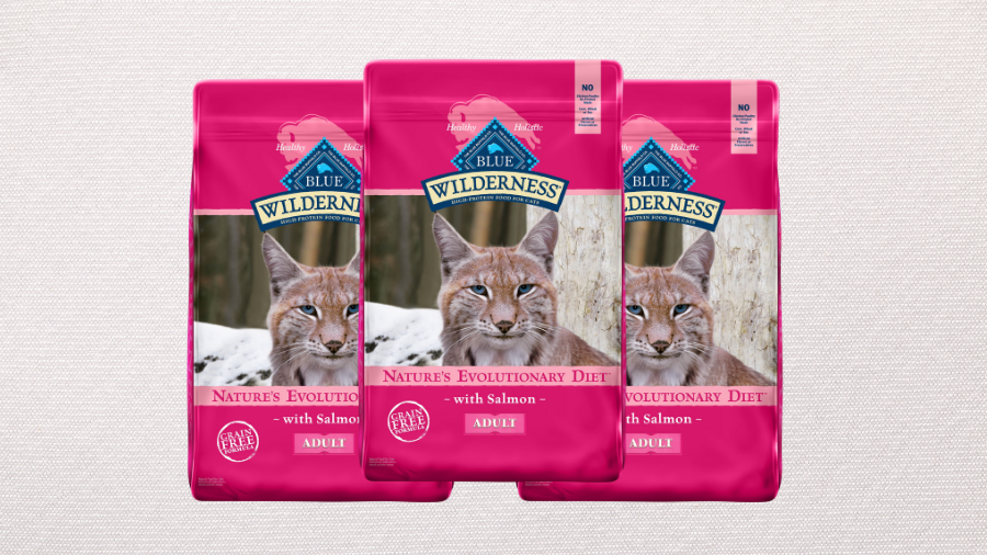 Three bags of Blue Wilderness Adult Cat Food with salmon, featuring a bold pink design and a wild cat image, displayed against a neutral textured background.