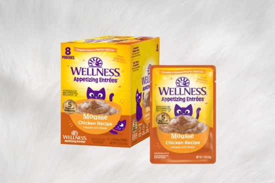 A box and pouch of Wellness Appetizing Entrées Mousse Chicken Recipe cat food, displayed against a soft white fur background.