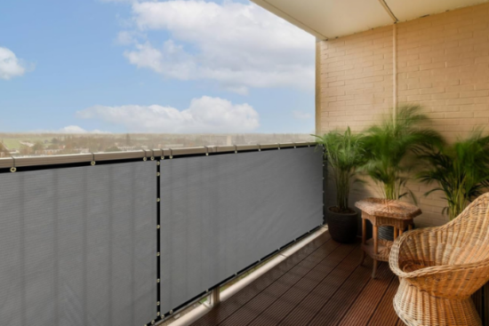 A cozy balcony with a privacy screen, rattan chair, and potted plants, offering a relaxing outdoor space with a scenic view.