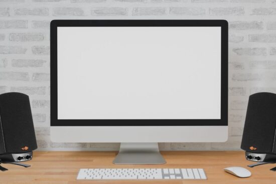 A computer with two black Klipsch ProMedia 2.1 speakers on a wooden desk.