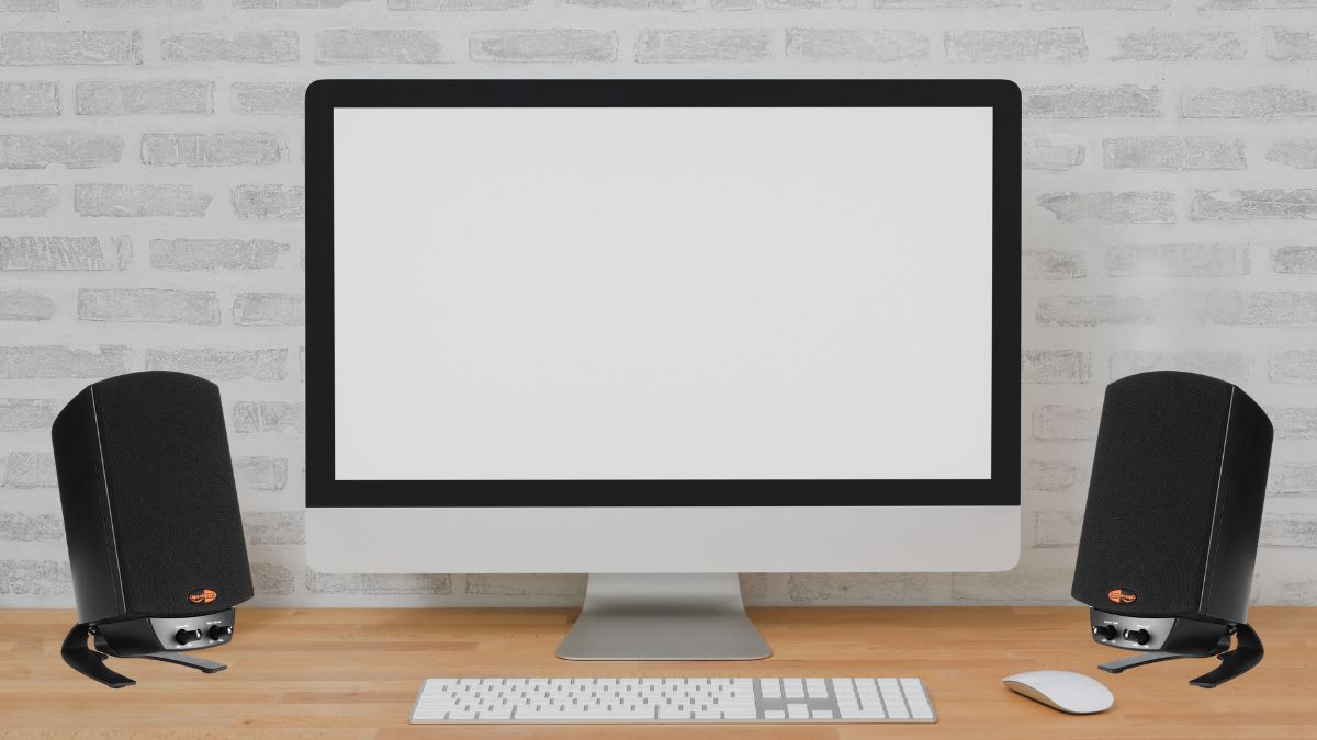 A computer with two black Klipsch ProMedia 2.1 speakers on a wooden desk.