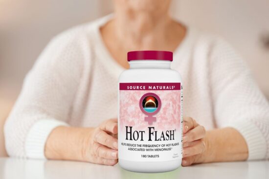 A person is holding a bottle of Source Naturals Hot Flash supplement with a pink label on a table.