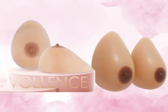 A set of Vollence silicone breast forms in different shapes and sizes, displayed on a pink stand with a soft background.