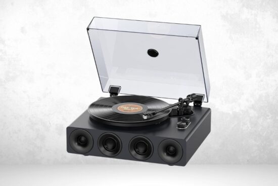 A black all-in-one turntable with built-in speakers, a clear dust cover, and a vinyl record playing on it.