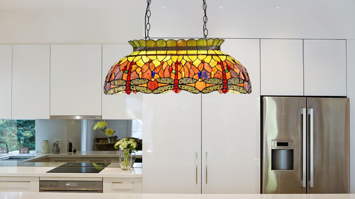 A stained glass pendant light with a dragonfly design hangs over a modern white kitchen island.