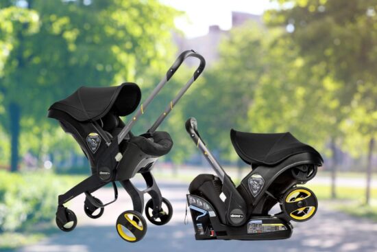 A black Doona car seat and stroller shown in both car seat mode and stroller mode on a park pathway with green trees in the background.