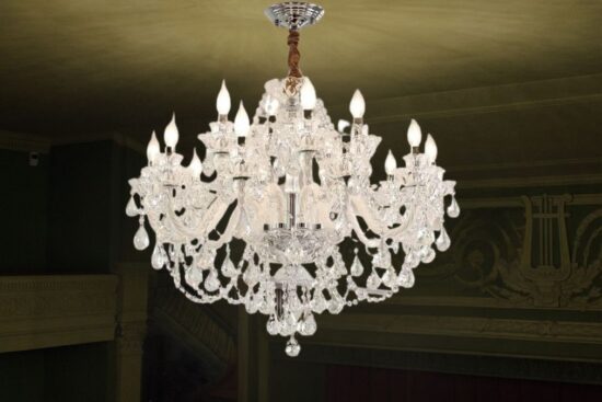 A grand clear crystal chandelier with multiple curved arms, candle-style lights, and hanging crystal drops, illuminating an elegant room with a classic design.