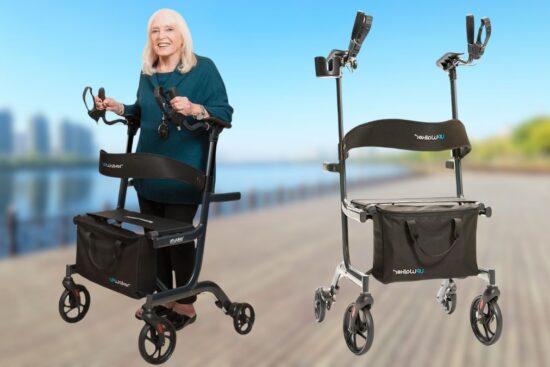 An elderly woman smiles while using a black UPWalker Lite, with another silver UPWalker Lite shown beside her on a boardwalk.
