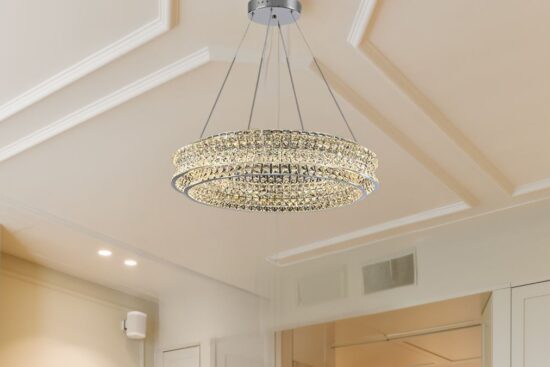 A modern crystal chandelier with two glowing rings hangs from the ceiling in a bright, stylish room.