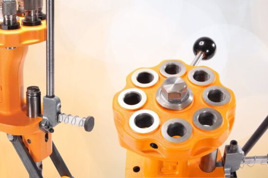 An orange 8-station turret press with multiple die slots, a black handle, and a sturdy metal frame is shown in close-up.