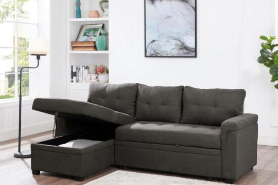 A dark gray sectional sofa with a pull-out sleeper and built-in storage, placed in a bright living room with large windows.