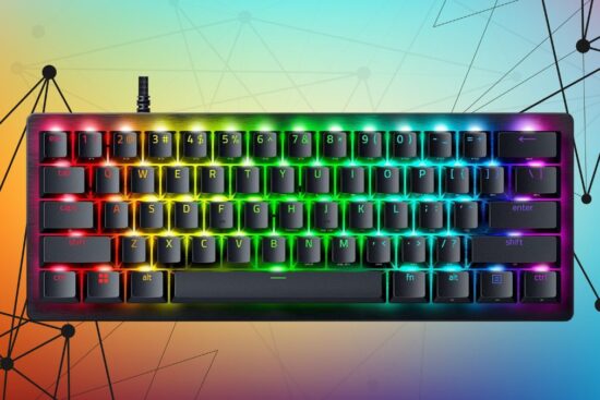 A compact gaming keyboard with RGB lighting, black keycaps, and a brushed metal top, glowing in a rainbow pattern.