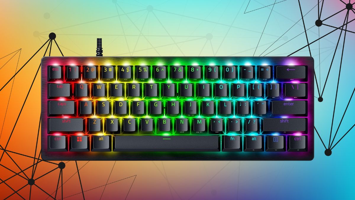 A compact gaming keyboard with RGB lighting, black keycaps, and a brushed metal top, glowing in a rainbow pattern.