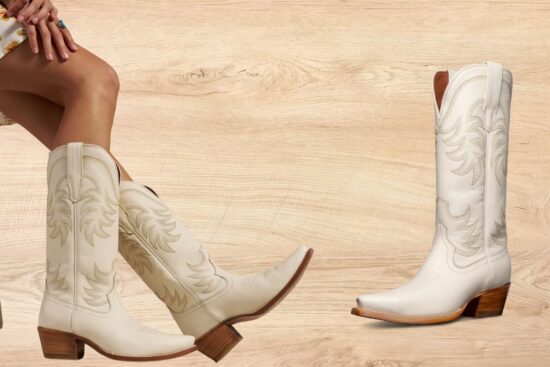 A pair of tall, cream-colored cowgirl boots with detailed stitching, a snip toe, and a stacked heel, worn by a woman sitting on a wooden stool.