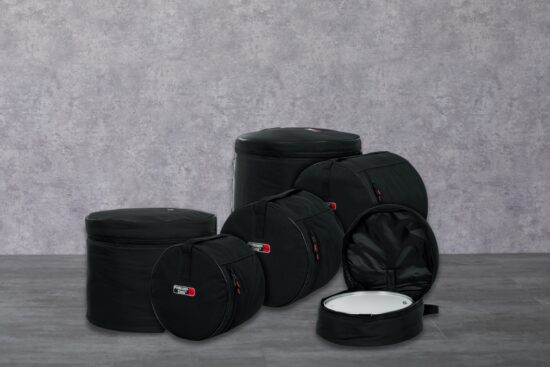 A set of black drum cases of different sizes is placed on a gray floor with one case open, showing a white drum inside.