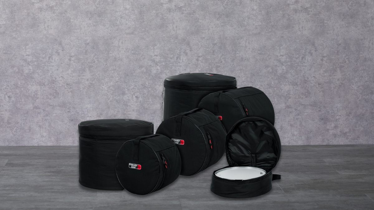 A set of black drum cases of different sizes is placed on a gray floor with one case open, showing a white drum inside.