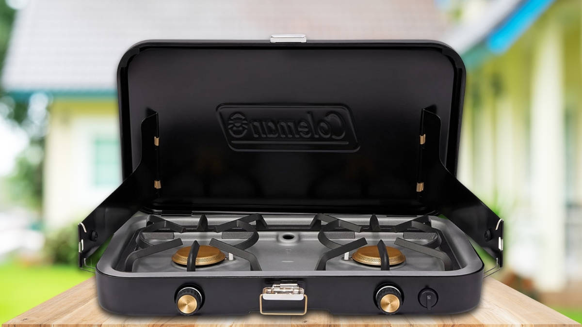A black Coleman portable gas stove with two burners, set up outdoors on a wooden surface.