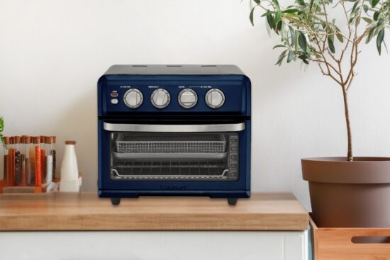 A blue air fryer toaster oven with dials sits on a kitchen counter next to spices and a potted plant.