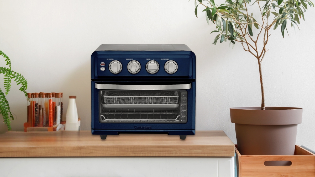 A blue air fryer toaster oven with dials sits on a kitchen counter next to spices and a potted plant.