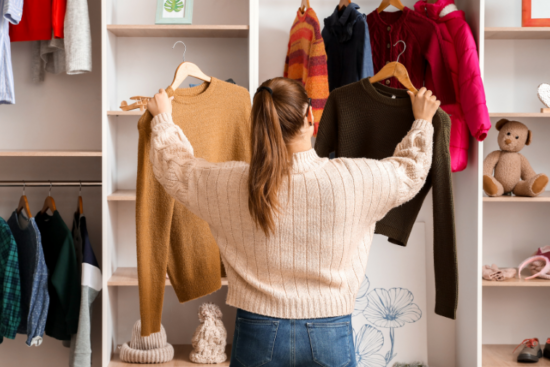A woman in a cream sweater holding up two knit sweaters, deciding between them in a cozy clothing store.