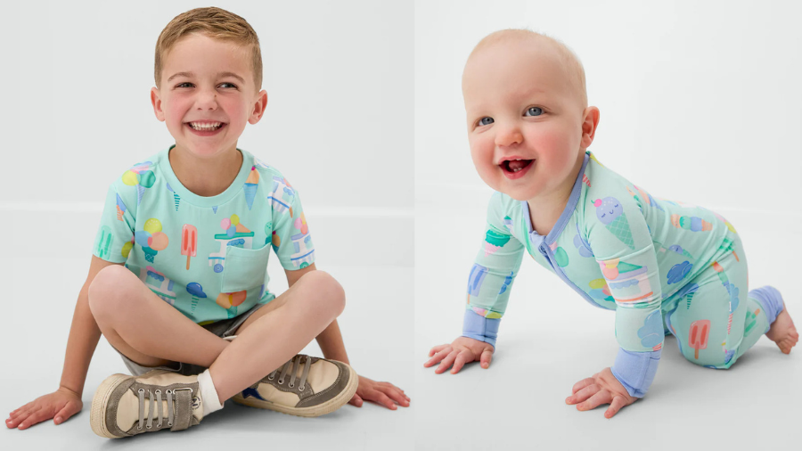 A smiling young boy in a mint green shirt with popsicle graphics, sitting cross-legged next to a crawling baby in a matching ice cream-themed onesie.