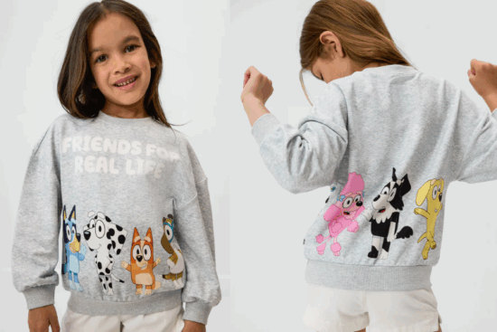 A young girl modeling a gray sweatshirt with cartoon animal characters and the text “Friends For Real Life” on the front and more colorful characters on the back.