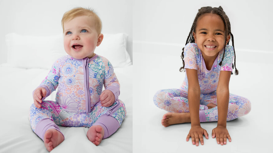 A baby and a young girl wearing matching pastel floral-patterned pajamas, sitting and smiling in a bright, white setting.
