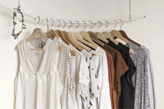 A clothing rack displaying a variety of neutral-toned garments hanging neatly on wooden hangers.