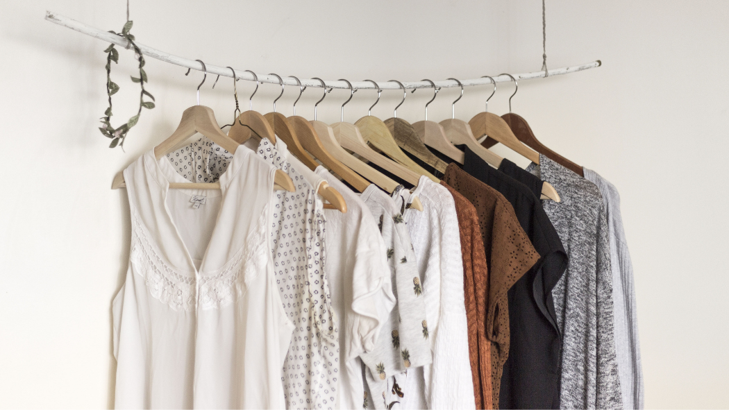 A clothing rack displaying a variety of neutral-toned garments hanging neatly on wooden hangers.