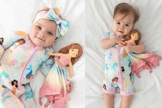 Two babies on a white bed, both wearing pastel pajamas with mermaid prints and each holding or cuddling a soft mermaid doll.
