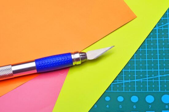 Precision craft knife on colorful cardstock sheets with a cutting mat used for paper crafting projects.