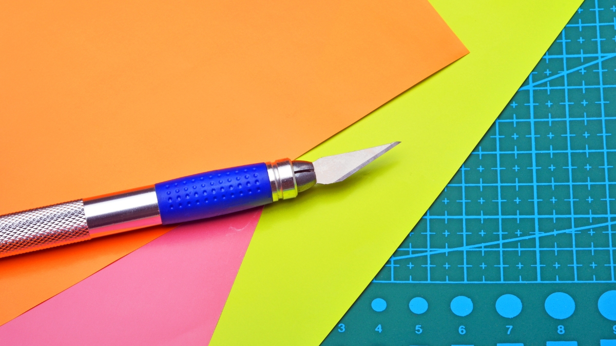 Precision craft knife on colorful cardstock sheets with a cutting mat used for paper crafting projects.