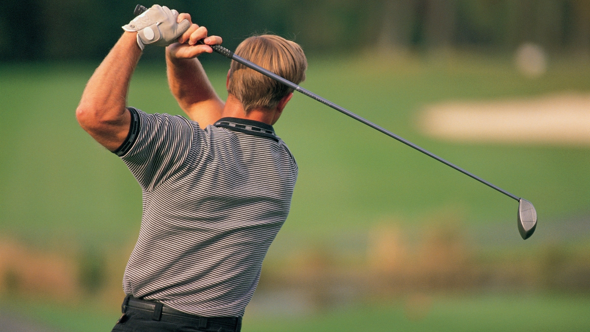 Man swinging a golf club on a green course during a sunny day.