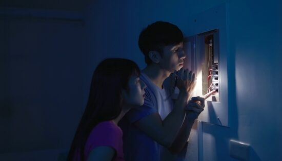 A couple checks the breaker box during a power outage, using a flashlight for light and CPAP battery backup for peace of mind.