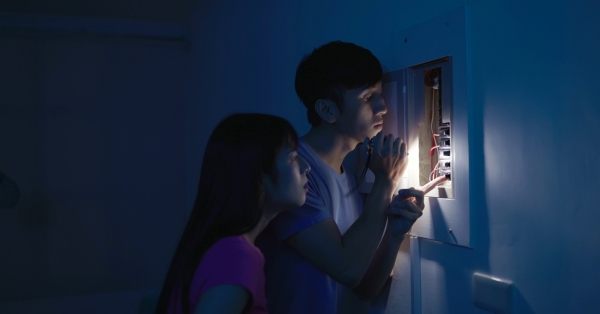 A couple checks the breaker box during a power outage, using a flashlight for light and CPAP battery backup for peace of mind.