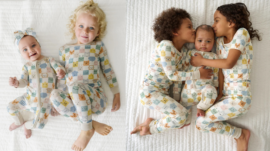 A group of children in matching pastel animal-print pajamas lying on a white quilt, smiling and cuddling.