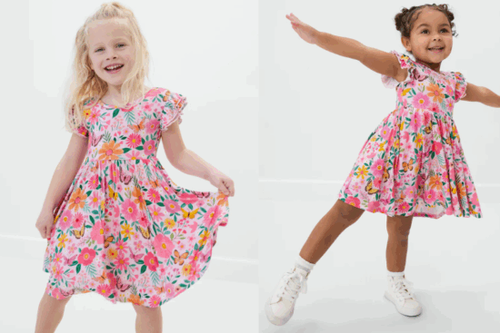 Two young girls wearing matching pink floral dresses, posing and twirling joyfully.