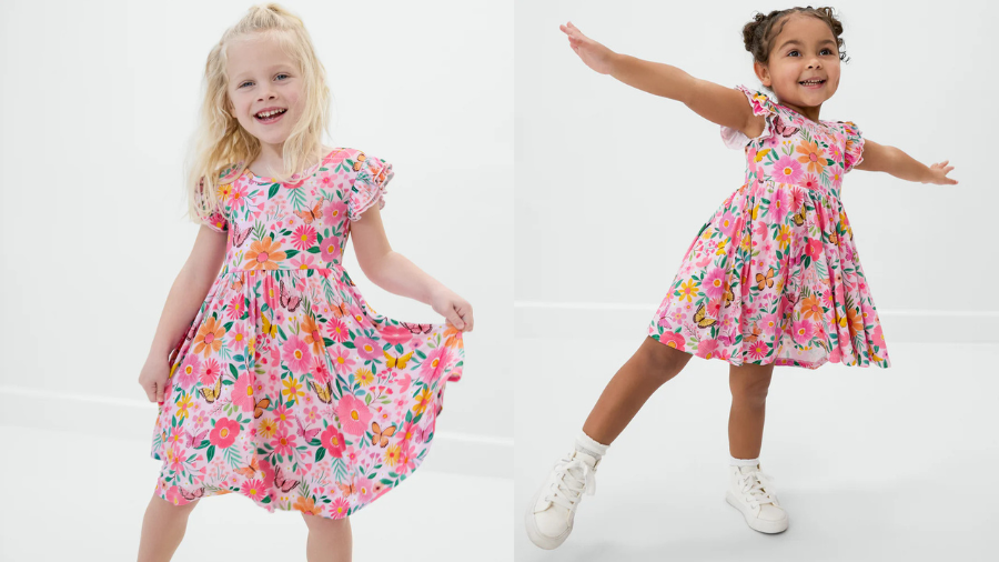 Two young girls wearing matching pink floral dresses, posing and twirling joyfully.