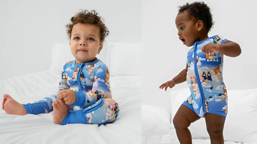 Two toddlers in blue character onesies, one sitting and one standing on a white bed.