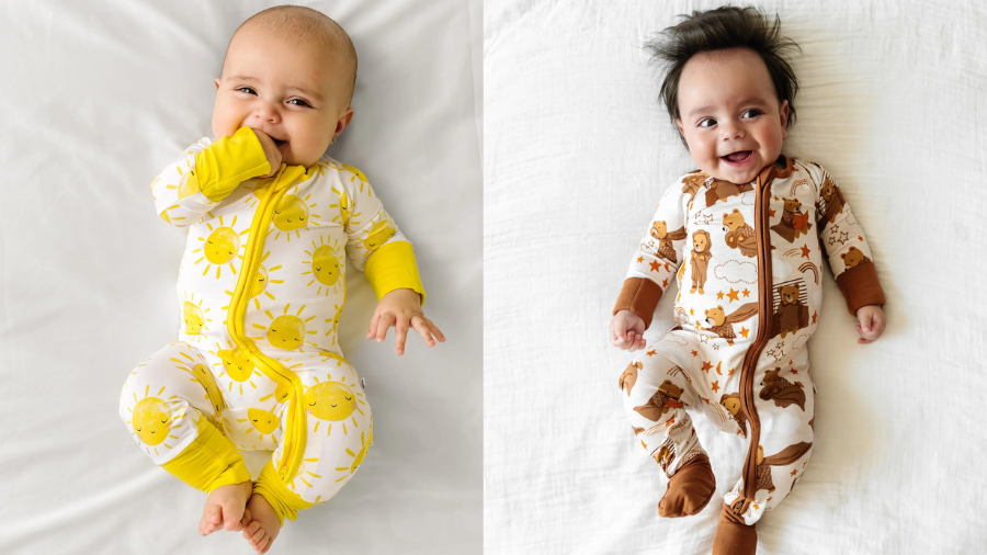 Two babies lying on white sheets, one in a yellow sun-patterned onesie and the other in a brown animal-themed onesie.