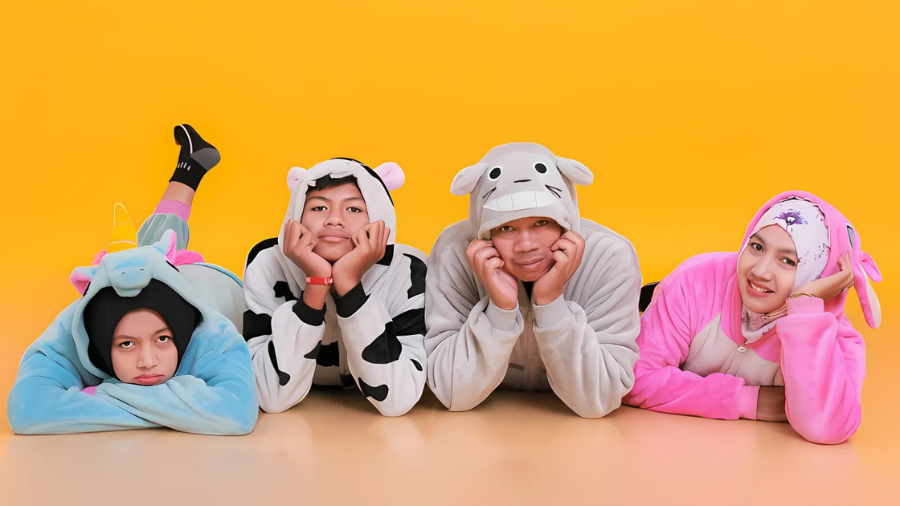 Four people wearing colorful animal-themed onesies posing playfully on the floor against a bright yellow background.