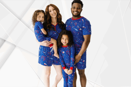 A smiling family wearing matching blue pajamas with red, white, and blue fireworks print for Independence Day.
