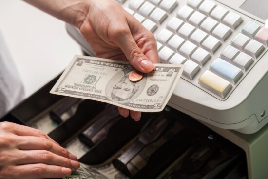 A cashier hands change to a customer at a cash register with an open cash drawer.