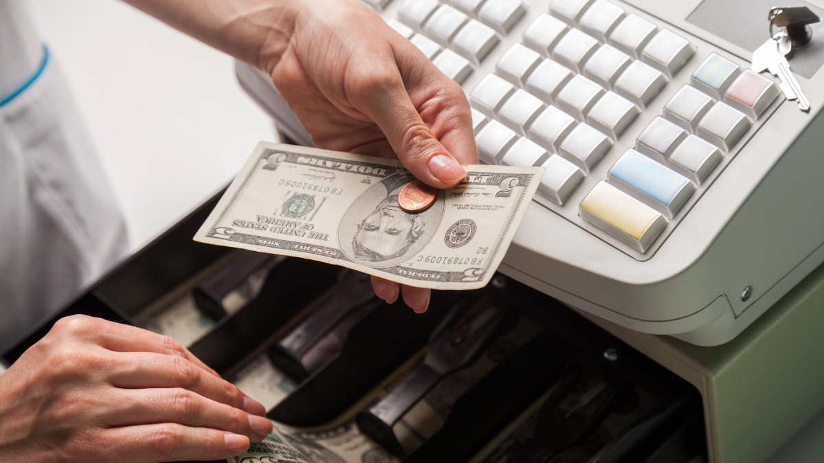 A cashier hands change to a customer at a cash register with an open cash drawer.