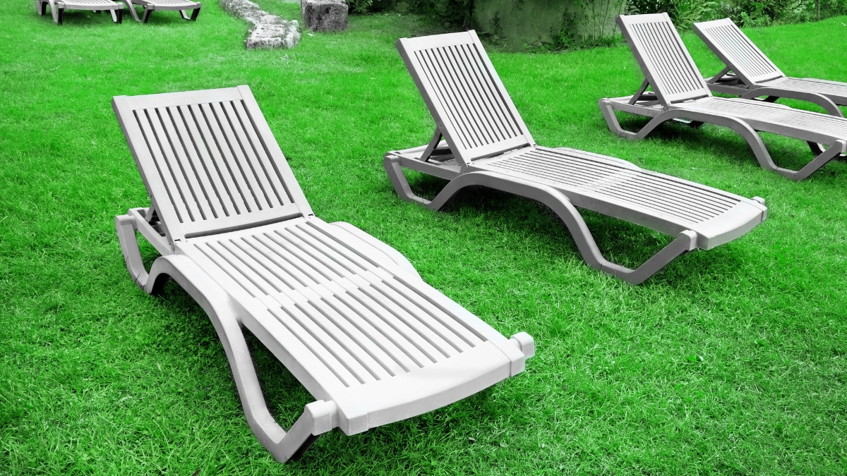 Several outdoor chaise lounge chairs are placed on a green lawn in a garden setting.