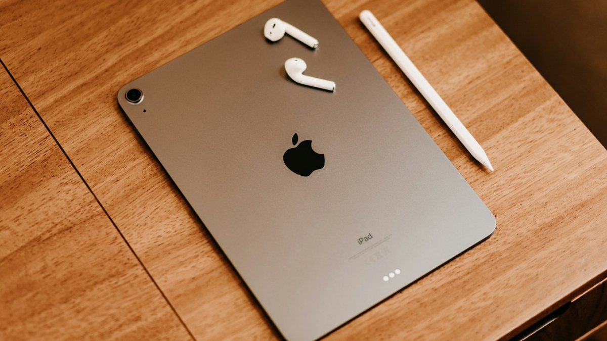 iPad Mini with Apple Pencil and AirPods placed on a wooden table.