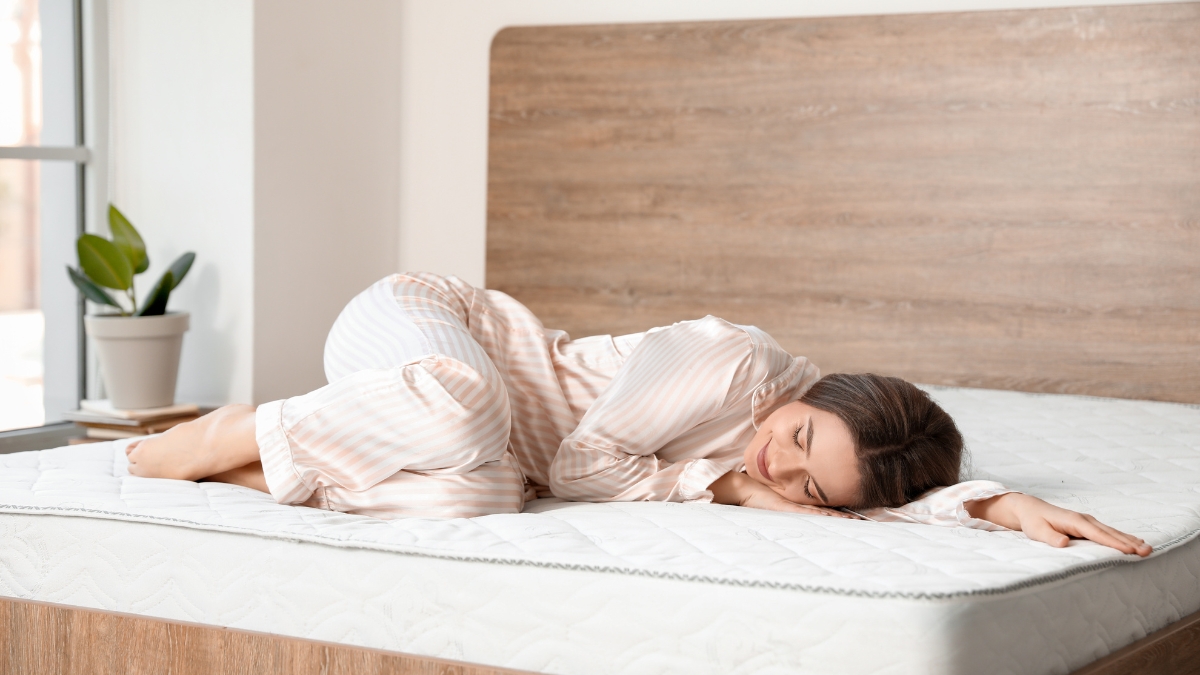 Woman sleeping comfortably on a gel memory foam hybrid mattress in a cozy, well-lit bedroom.