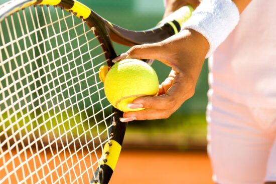 Close-up of a tennis player holding a ball and racket on a clay court during practice.